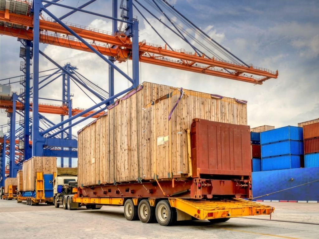 Trucks carrying wooden crates at a port with blue and orange cranes, a cargo ship, and containers.