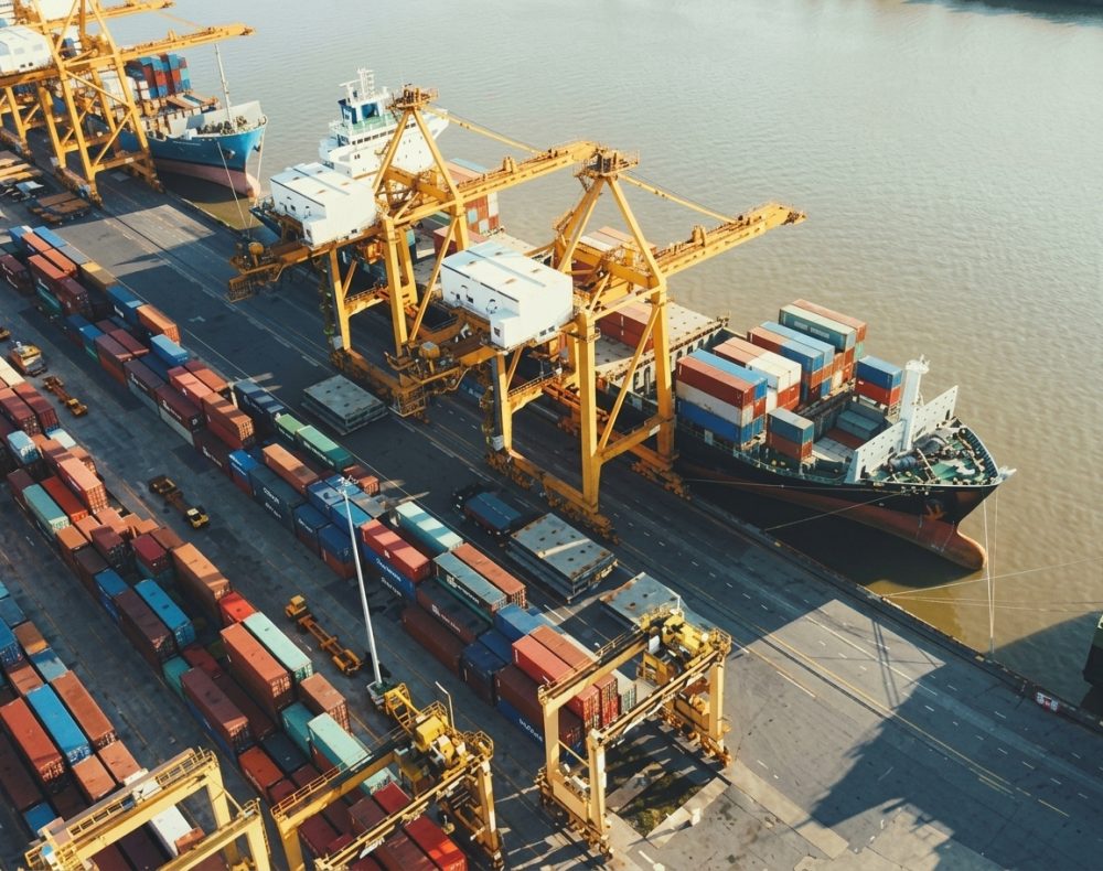 Aerial view of a cargo ship being loaded with shipping containers at a busy port with large cranes.
