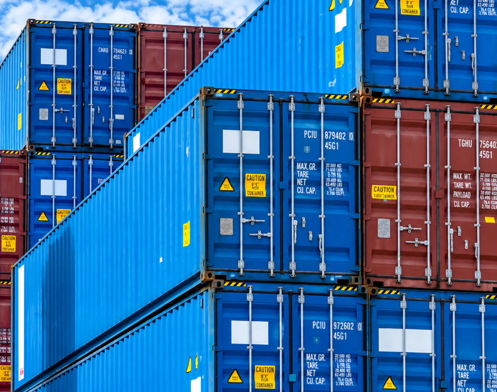 Blue and red shipping containers stacked at a port, blue sky in the background.
