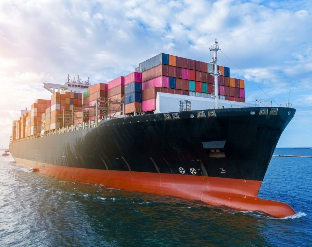 Cargo ship sailing on the ocean, loaded with shipping containers, blue sky.