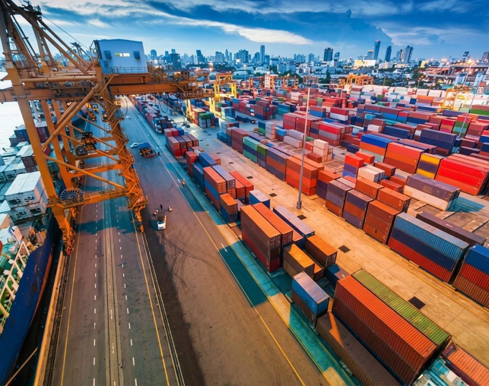 Shipping port with cargo containers, crane, and city skyline in the background.